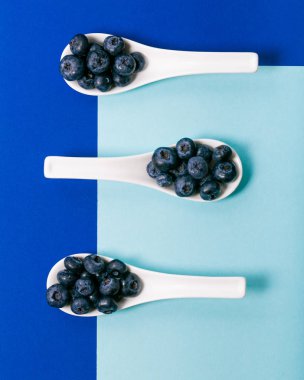 Mavi arka plan üzerinde beyaz kaşık üzerinde modern yaban mersini