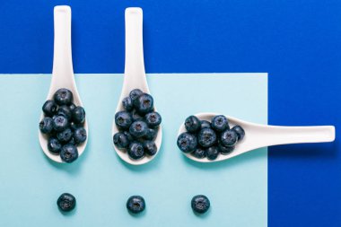 Mavi arka plan üzerinde beyaz kaşık üzerinde modern yaban mersini