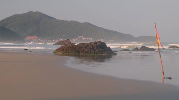 朝の岩と波の赤い旗のビーチの眺め — ストック動画