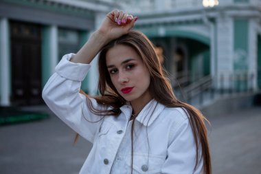 Çekici esmer portre. Kız eliyle saçına dokunuyor. Beyaz kot ceketli bir kız. Kırmızı ruj..