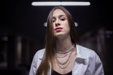 Geceleri lambaların altındaki bir geçitte genç bir kız. Beyaz kot ceketli bir esmer tünelde poz veriyor..