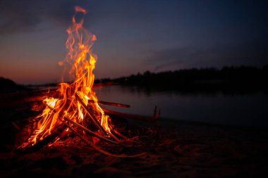 Gece nehir kıyısında şenlik ateşi. Yazın baraj gölünün yanında yanan dallardan ve yakacak odunlardan çıkan kırmızı alevler. Ateşin yanında açık hava eğlencesi..