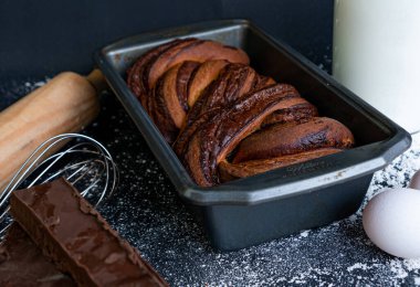 Lezzetli ev yapımı trenza ekmeği bir tarafında süt olan cam bir şişeyle kalıbın içinde bir masada bir parça çikolata ve siyah arka plan..