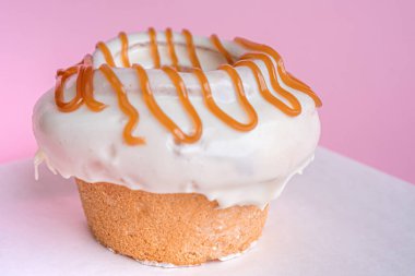 Süslü ev yapımı tarçınlı rulo, beyaz bir masaya yerleştirilmiş pembe arka planda karamel ile süslenmiş..