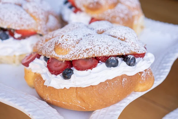 Delicious traditional Mexican pan de muerto or bread of dead made with orange filled with whipped cream and red fruits on a white Mexican style plate.
