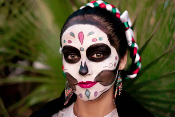 Young Mexican woman with colorful traditional Day of the Dead skull makeup and traditional Mexican dress.