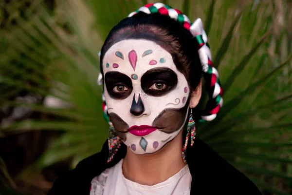 Young Mexican woman with colorful traditional Day of the Dead skull makeup and traditional Mexican dress.