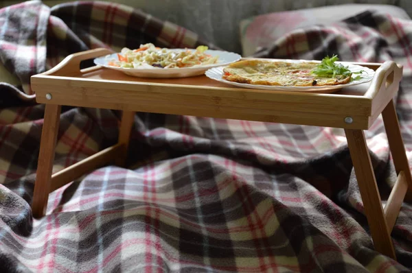Yummy romantic breakfast in bed on bamboo food-tray on cosy checkered plaid. Omelette with fresh salat. Health food concept. Stay at home during quarantine. Save lives