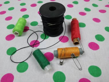 Nakış için farklı renkte iplikler, masanın üzerinde bir makara iplik, iğne ve iğne var.
