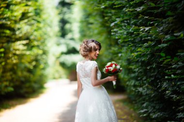 Parkta yeşillik arka planında düğün buketi olan esmer gelin.