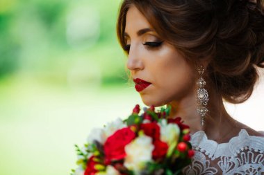 Parkta yeşillik arka planında düğün buketi olan esmer gelin.