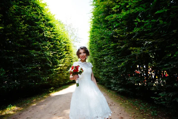 Die Braut im weißen Brautkleid hält einen Strauß vor einem grünen Park — Stockfoto