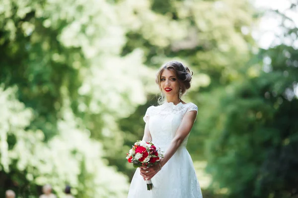 A noiva em um vestido de casamento branco mantém um buquê em um fundo de parque verde — Fotografia de Stock