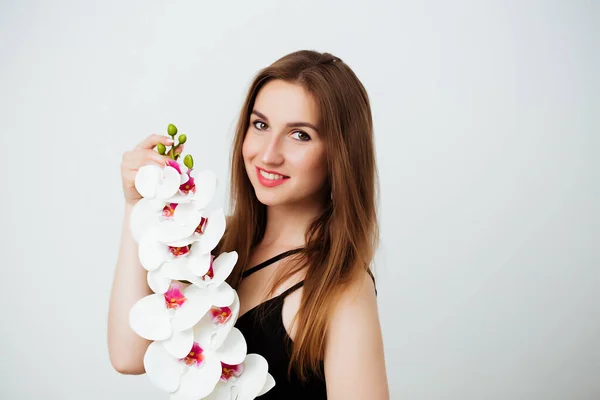 Ung kvinna som håller orkidé blomma på vit bakgrund i studio. Flickan tittar på kameran. Närbild — Stockfoto