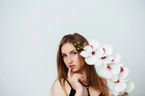 Mladá žena drží orchidej květiny na bílém pozadí ve studiu. Dívka se dívá do kamery. Zavřít — Stock fotografie