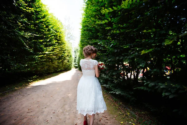 Die Braut im weißen Brautkleid hält einen Strauß vor einem grünen Park — Stockfoto