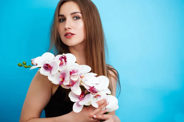 Junge Frau mit Orchideenblume auf weißem Hintergrund im Atelier. Das Mädchen blickt in die Kamera. Nahaufnahme — Stockfoto