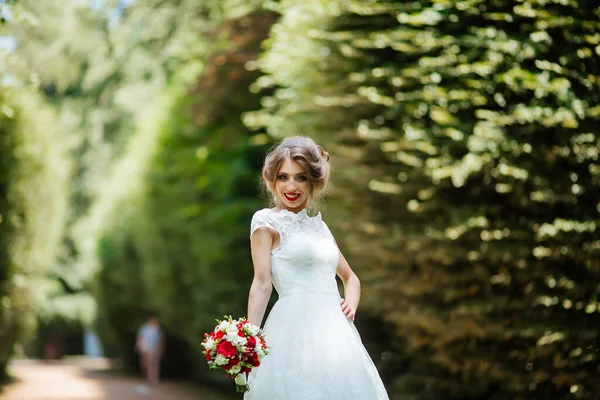 Mooie bruid met een bruiloft boeket in haar handen buiten in het park. — Stockfoto