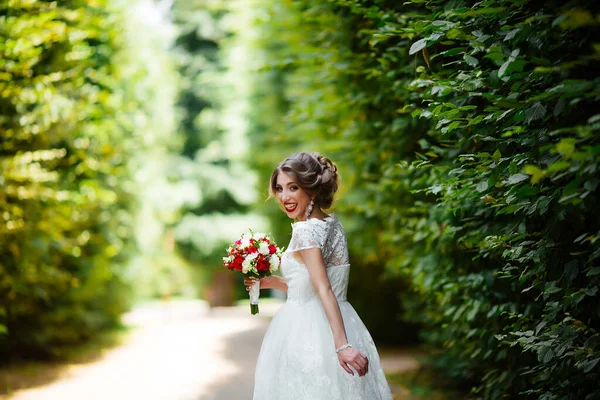 Брюнетка наречена в сукні з весільним букетом в парку на фоні зелені — стокове фото