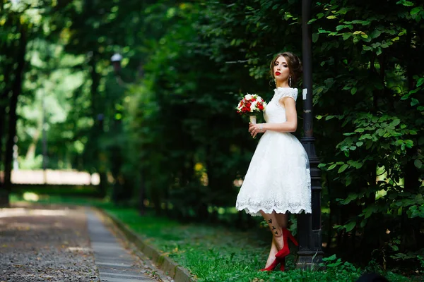 Брюнетка наречена в сукні з весільним букетом в парку на фоні зелені — стокове фото