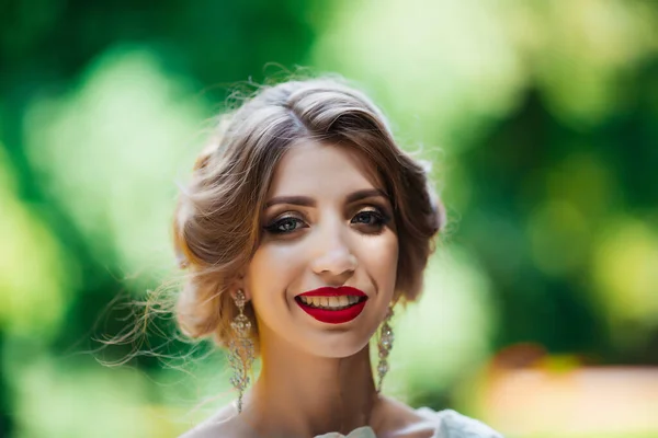 A noiva em um vestido de casamento branco mantém um buquê em um fundo de parque verde — Fotografia de Stock