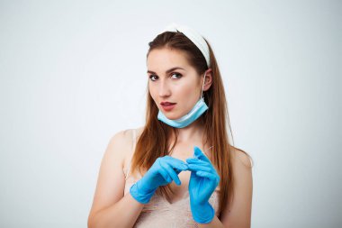 Siyah saçlı doktor kız, beyaz stüdyo arka planında mavi eldiven ve tıbbi maske takıyor ve elinde şırınga, portre, güzellik tedavisi tutuyor..
