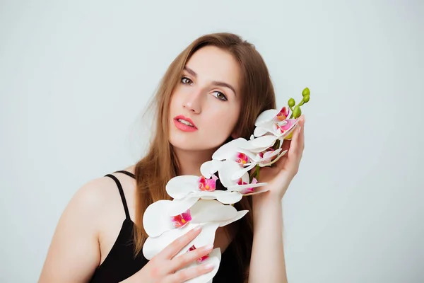 Junge Frau mit Orchideenblume auf weißem Hintergrund im Atelier. Das Mädchen blickt in die Kamera. Nahaufnahme — Stockfoto