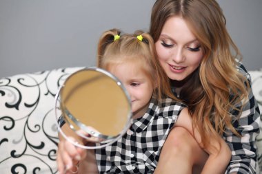 Neşeli gülümseyen mutlu anne ve küçük meraklı kızı yatakta yatıyor.