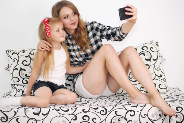 Beautiful mom and daughter are photographed on the phone in bed, happy family — Stock Photo, Image