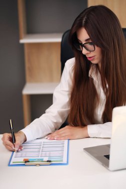 İşine odaklan. Genç ve güzel bir kadın iş yerinde bir sandalyede otururken bilgisayarını kullanıyor.