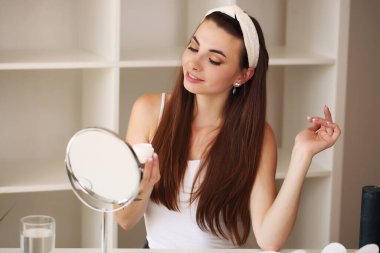Genç ve güzel esmer cilt bakımı evde aynanın yanında.