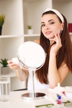 Güzellik, cilt bakımı ve insan konsepti. Gülümseyen genç kız, odadaki yüz için güzellik öneriyor.