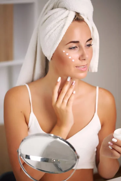 Potret seorang wanita cantik menerapkan krim wajah untuk perawatan kulit — Stok Foto