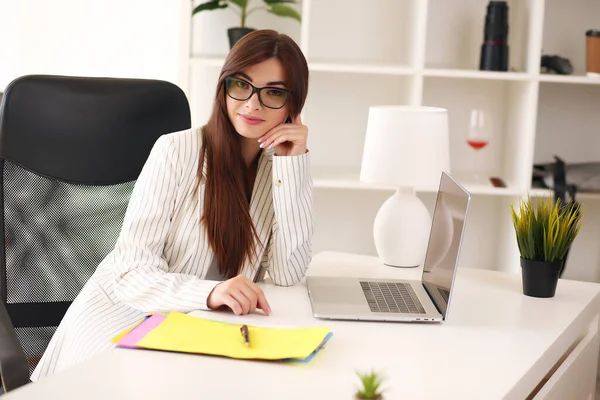 Mulher de negócios bonita usa um laptop e sorri enquanto trabalha no escritório — Fotografia de Stock