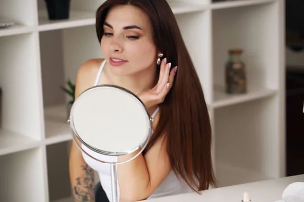 Schoonheid, huidverzorging jonge vrouw aanbrengen gezichtscrème en kijken in spiegel in huis badkamer. — Stockfoto