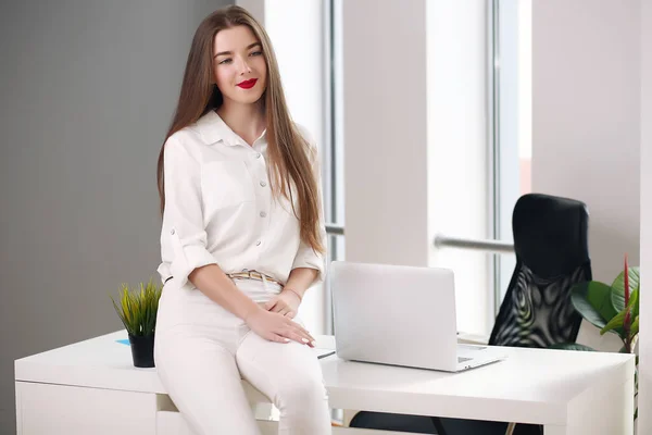 Jovem sentada em uma mesa com um laptop em um escritório branco. estudante ou empresária — Fotografia de Stock