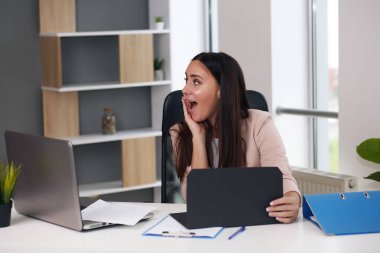 Yükseltilmiş el hareketi yapan mutlu bir iş kadını. Masada dizüstü bilgisayarın önünde el hareketleriyle mektup okuyor. İş adamı yazışmalardan gelen iyi haberlerden memnun..