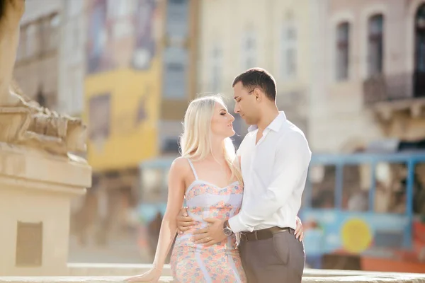 Una bella coppia che gira per l'isolato. Uomo dai capelli scuri in camicia bianca che abbraccia una bionda in un bellissimo vestito — Foto Stock