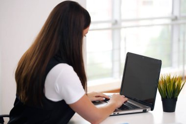Laptop bilgisayarında çalışan çekici, gülümseyen genç bir kız.