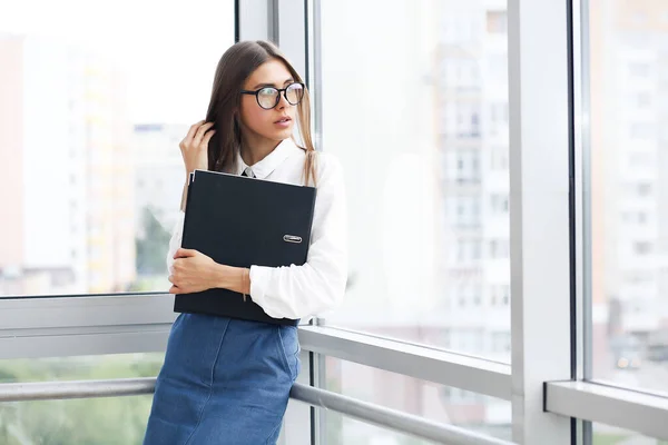 Confident business expert. Attractive young smiling woman in business clothes leaning on office window