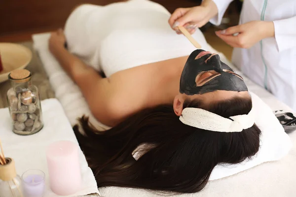 Κοντινό πλάνο του αγνώριστη κοσμητολόγος εφαρμογή μάσκα προσώπου με βούρτσα στο πρόσωπο της όμορφης γυναίκας που βρίσκεται στο τραπέζι μασάζ στο κέντρο SPA — Φωτογραφία Αρχείου