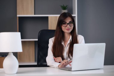 Ofisinde dizüstü bilgisayar kullanan genç bir iş kadını.