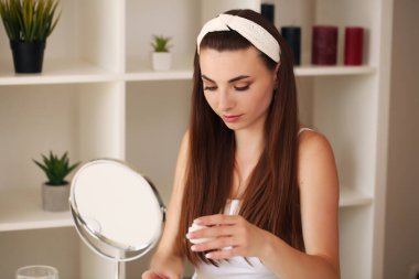 Evde oturuyor, aynaya bakıyor, gülüyor ve eğleniyor. Sabah cilt bakım rejimi.