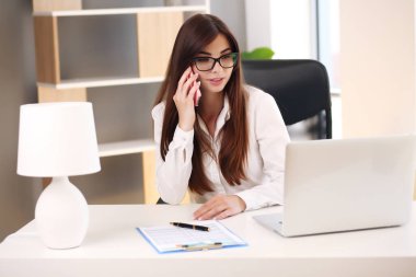 Güzel bir iş kadını ofiste çalışırken dizüstü bilgisayar kullanır ve gülümser.