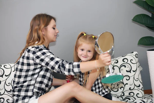 Madre e hija están sentadas en la cama en el dormitorio. Feliz familia amorosa. Madre e hija hacen el pelo, maquillaje — Foto de Stock