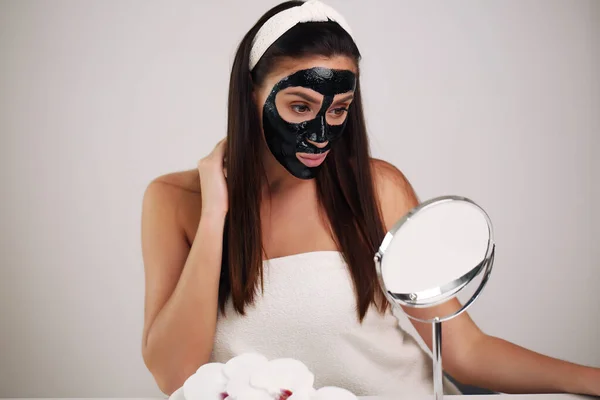 Młoda kobieta z czarną maską detoksykacyjną na twarzy, nastolatka dba o tłustą skórę, oczyszczając pory. Salon piękności. Skóra. — Zdjęcie stockowe