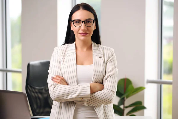 Chica de negocios en un traje de pie en la mesa, brazos cruzados — Foto de Stock