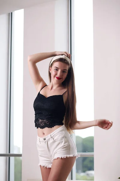 Hermosa joven morena con el pelo largo de pie en una camiseta y pantalones cortos de mezclilla —  Fotos de Stock