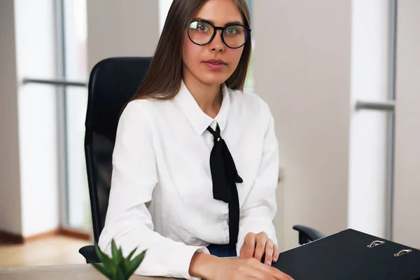 Молодая деловая леди, сидящая в кресле, работая, держа папку с документами — стоковое фото
