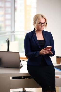 Genç sarışın iş kadını ofiste masa başında oturuyor.